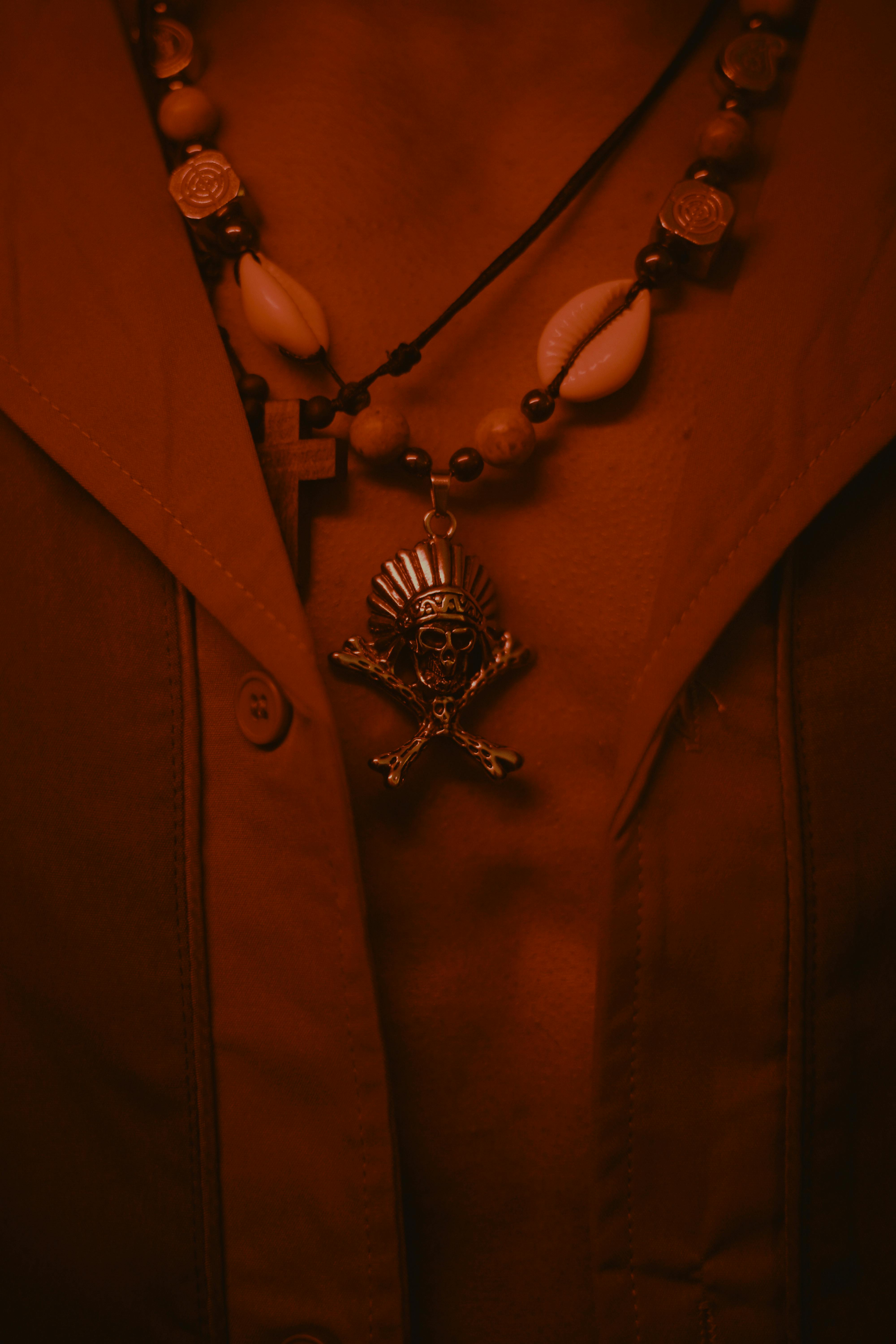 Gratis Ripresa dettagliata di collane tribali e a croce su una camicia abbottonata sotto una luce calda. Foto a disposizione