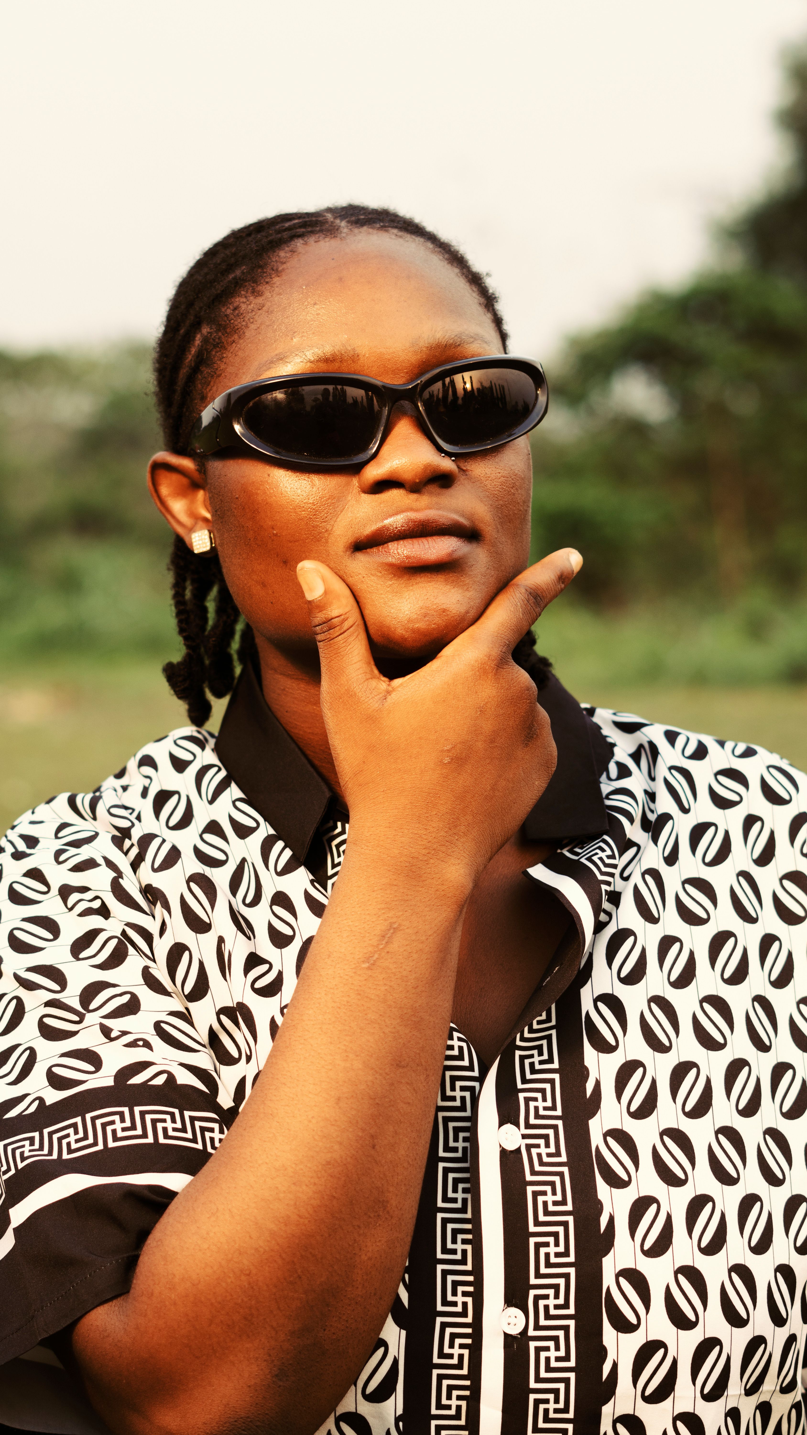 Young woman striking a thoughtful pose with sunglasses in an outdoor setting.