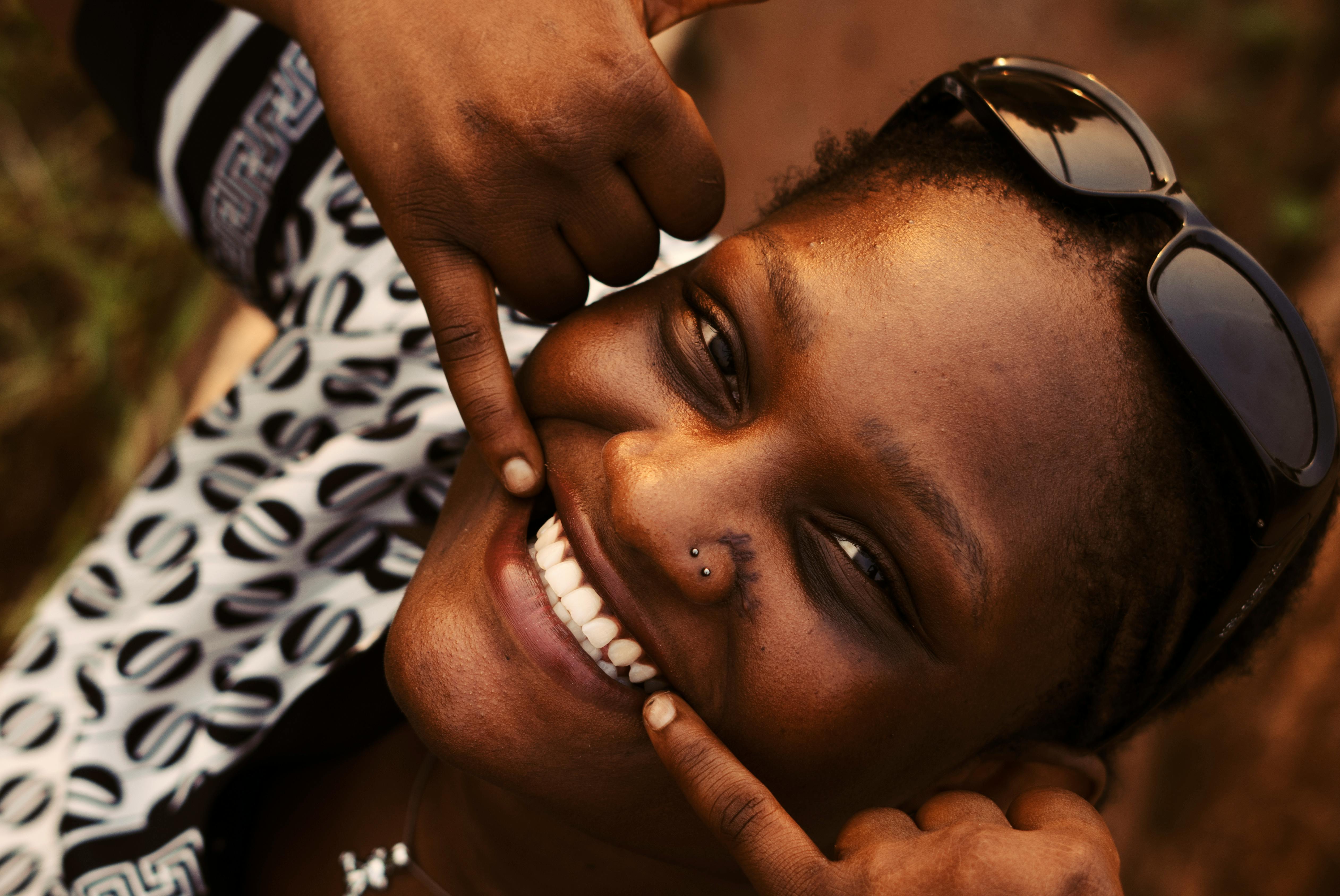 Gratis Una donna sorridente posa giocosamente all'aperto con gli occhiali da sole. Foto a disposizione