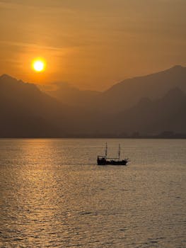 Captivating sunset over the Mediterranean Sea with a lone boat silhouette and mountains in Antalya, Turkey.