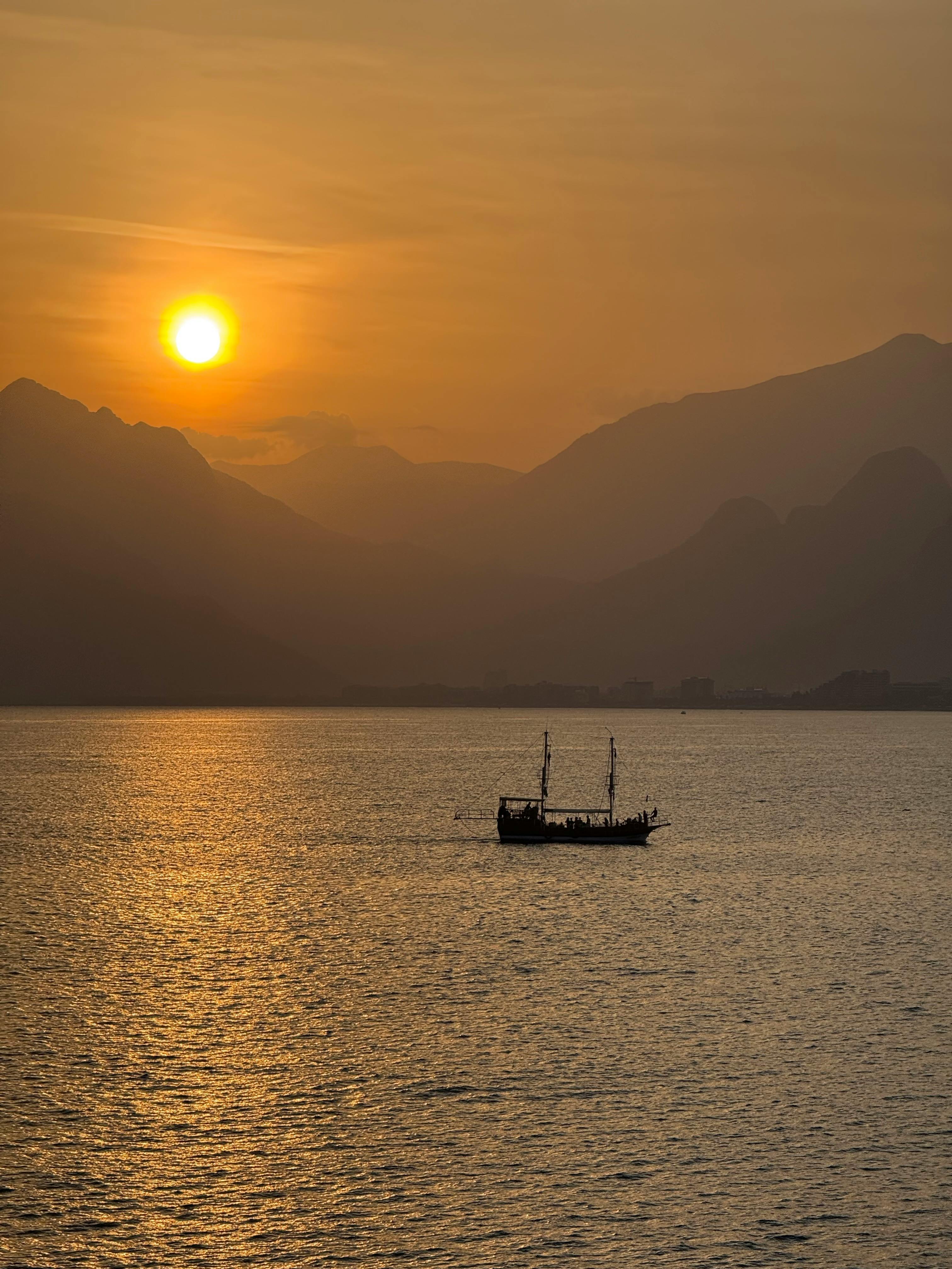 gratis Een betoverende zonsondergang boven de Middellandse Zee met het silhouet van een eenzame boot op de achtergrond en de bergen in Antalya, Turkije. Stockfoto