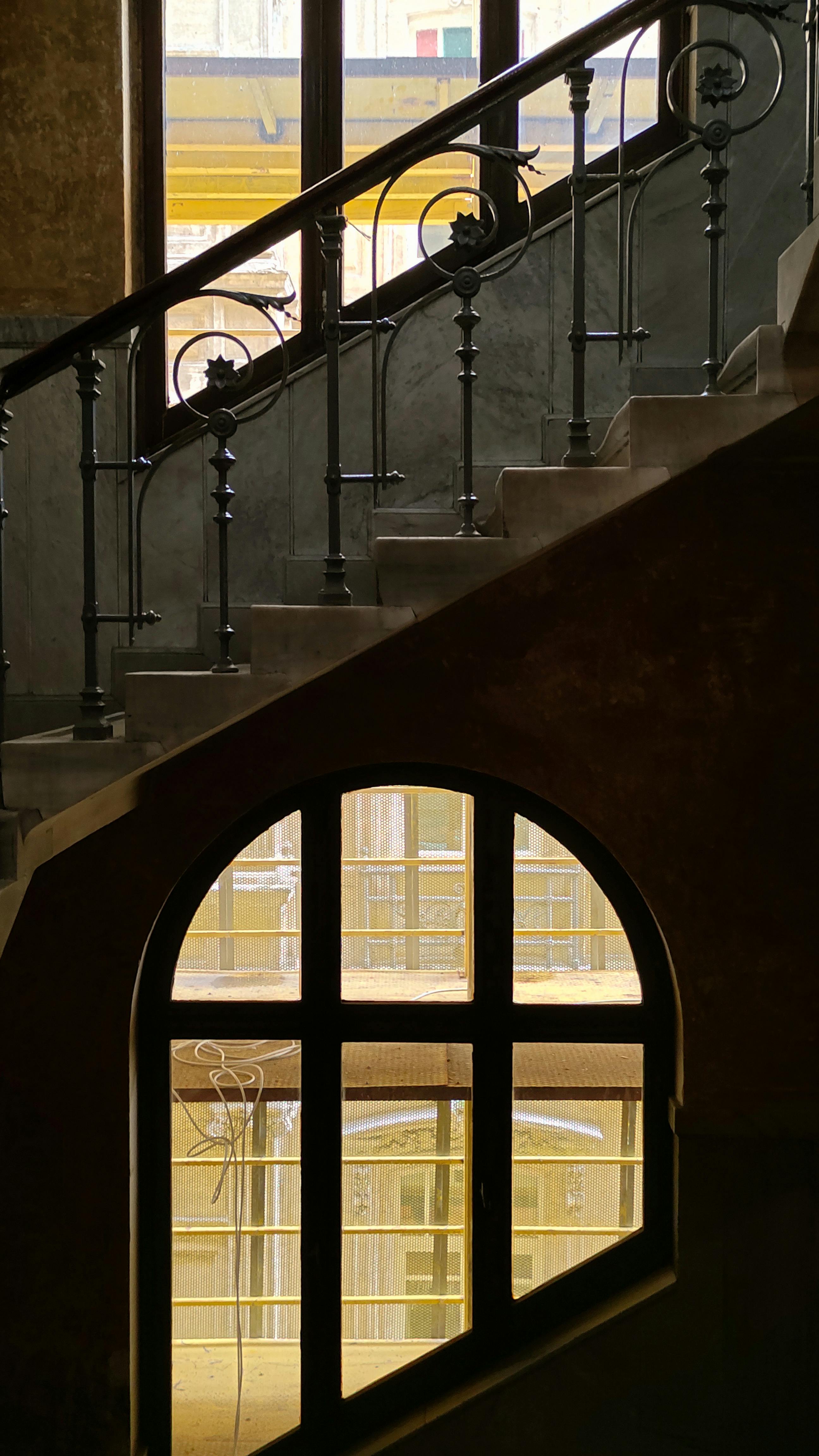 Gratuit O scară clasică cu fierărie complexă și fereastră arcuită, surprinsă în interior. Fotografie de stoc