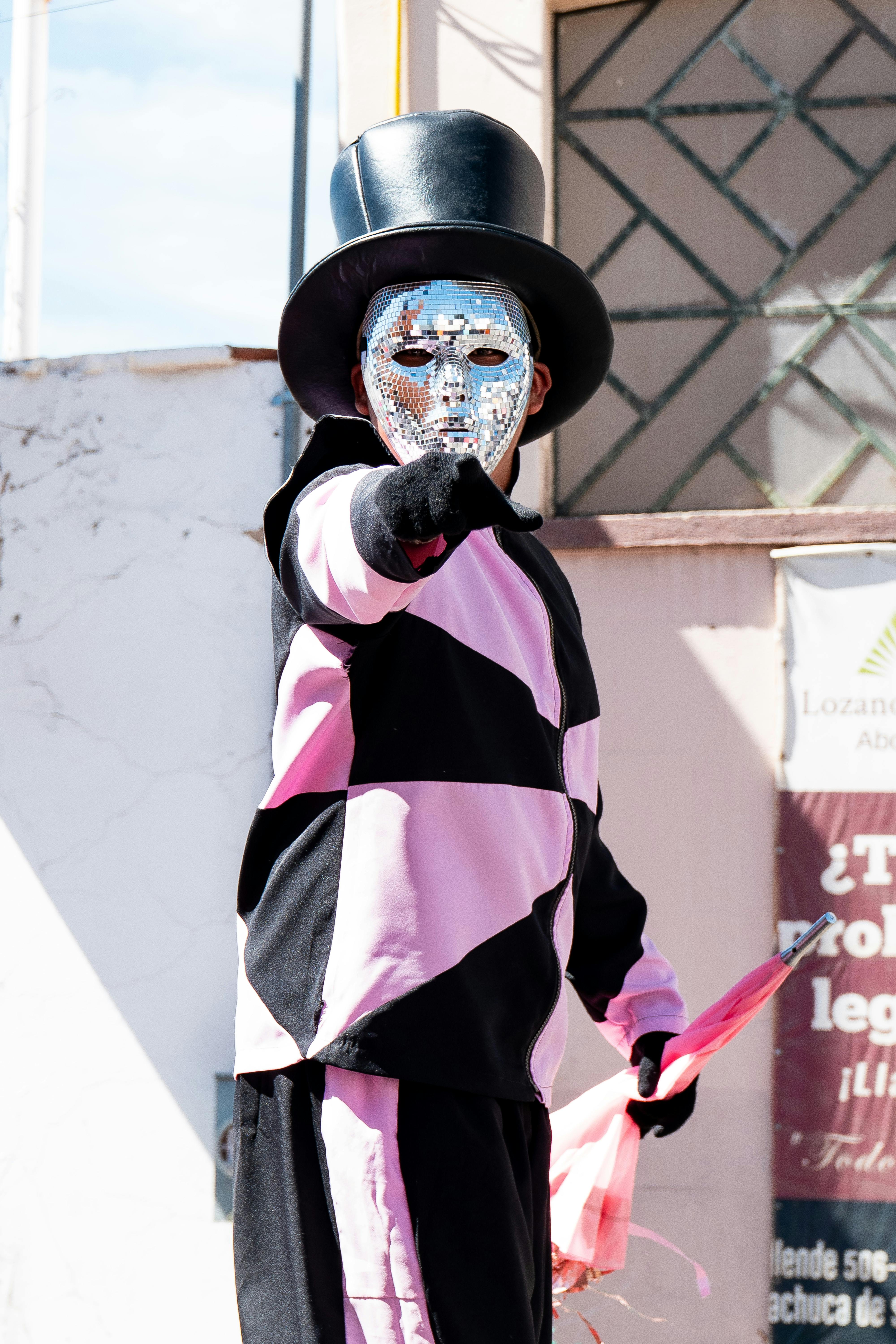 Gratuit Artiste de rue en costume rose et noir, portant masque et haut-de-forme, en extérieur. Photos