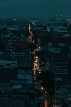 A moody nighttime view of a city under rainy conditions with glistening street lights.