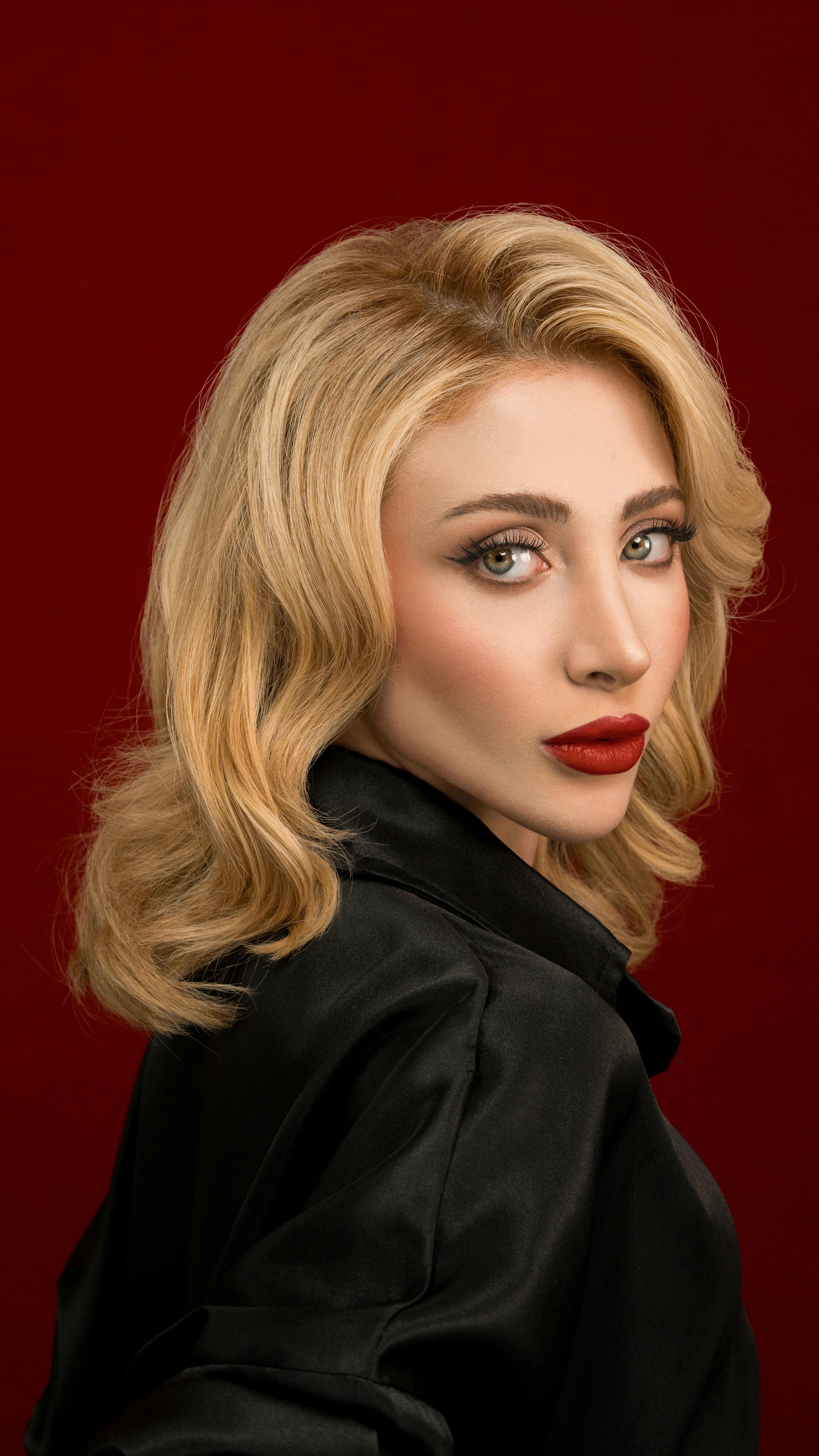 bezplatná Stylový portrét ženy s blond vlasy a červenými rty na červeném pozadí. Základová fotografie