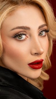 Close-up portrait of woman with stunning makeup and blonde hair on red background.