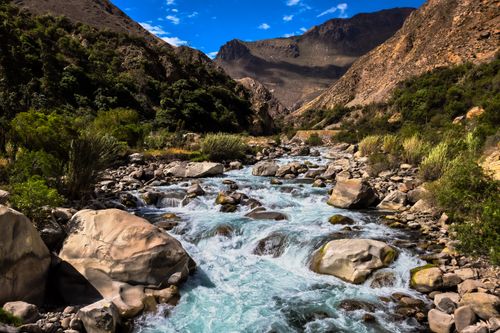 Free A picturesque mountain river flowing through a rugged landscape with lush greenery and rocky terrain. Stock Photo