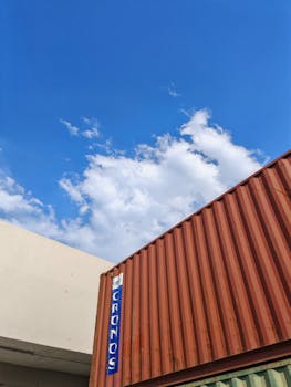 Industrial shipping container under a bright blue sky with clouds.