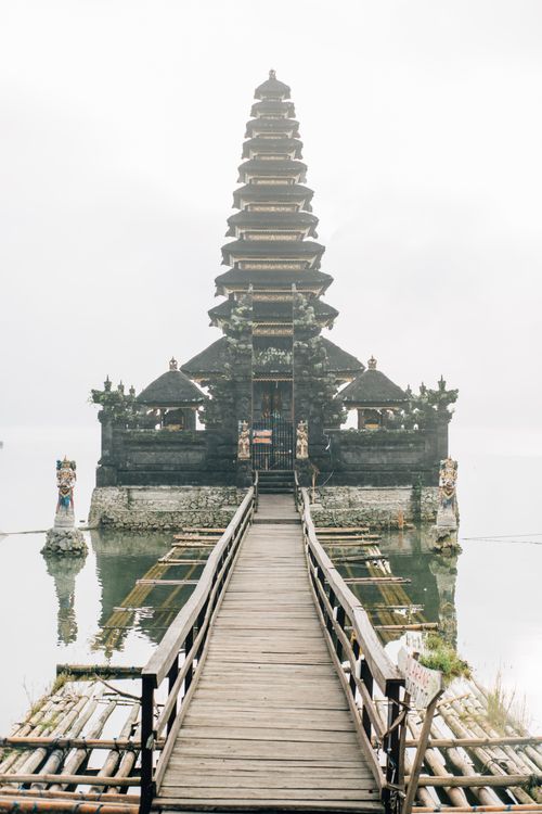 Free Beautiful Balinese temple on a misty lake with a wooden footbridge leading to it. Stock Photo