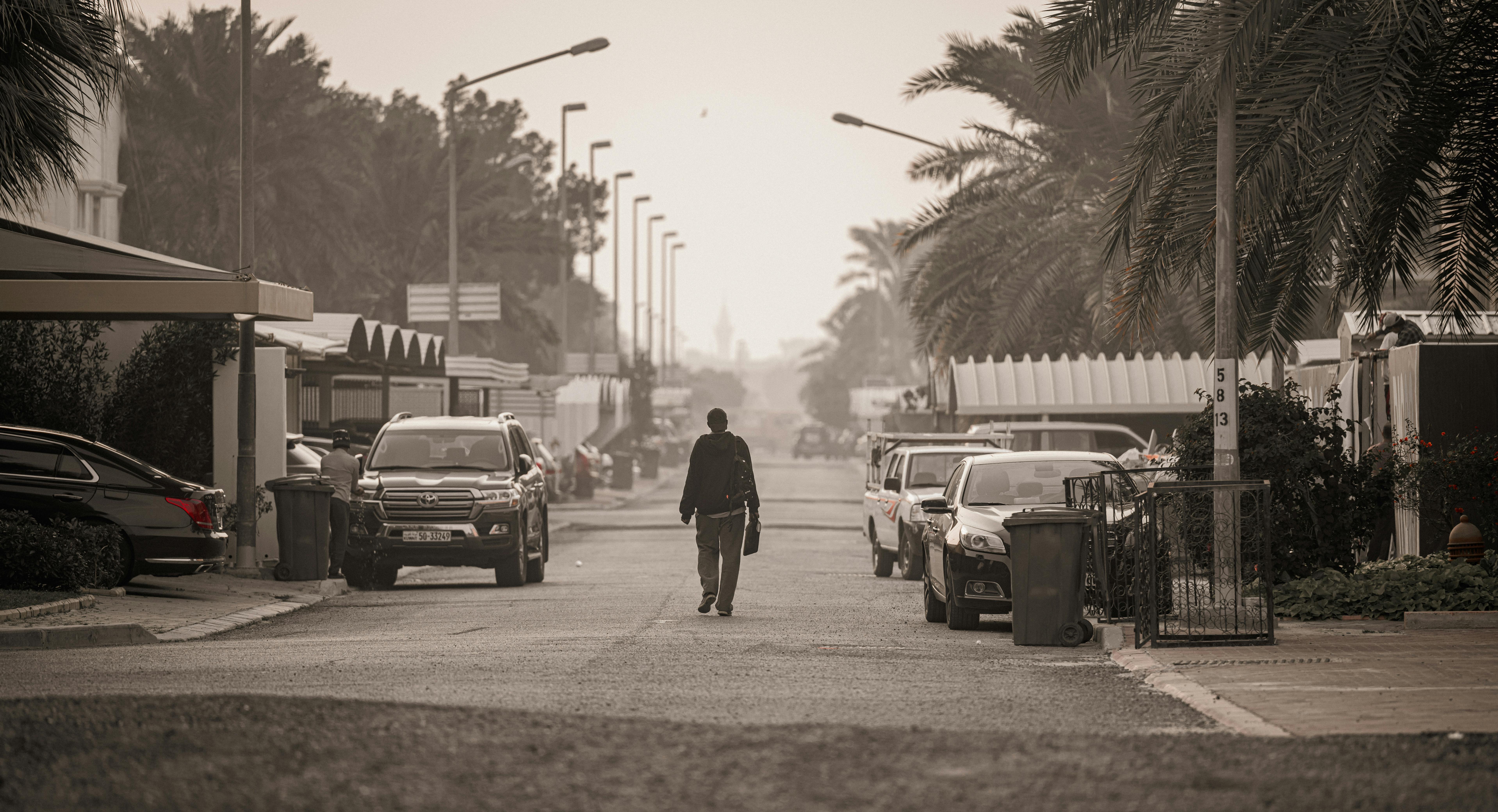 免费 一名男子走在科威特城的一条居民街道上，周围是汽车和棕榈树。 素材图片