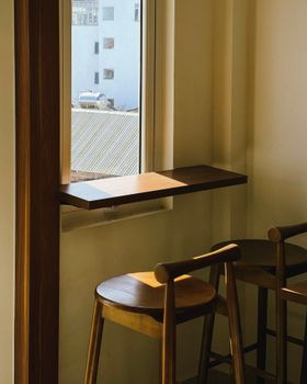 A warm, minimalist cafe interior with wooden chairs by a sunlit window.