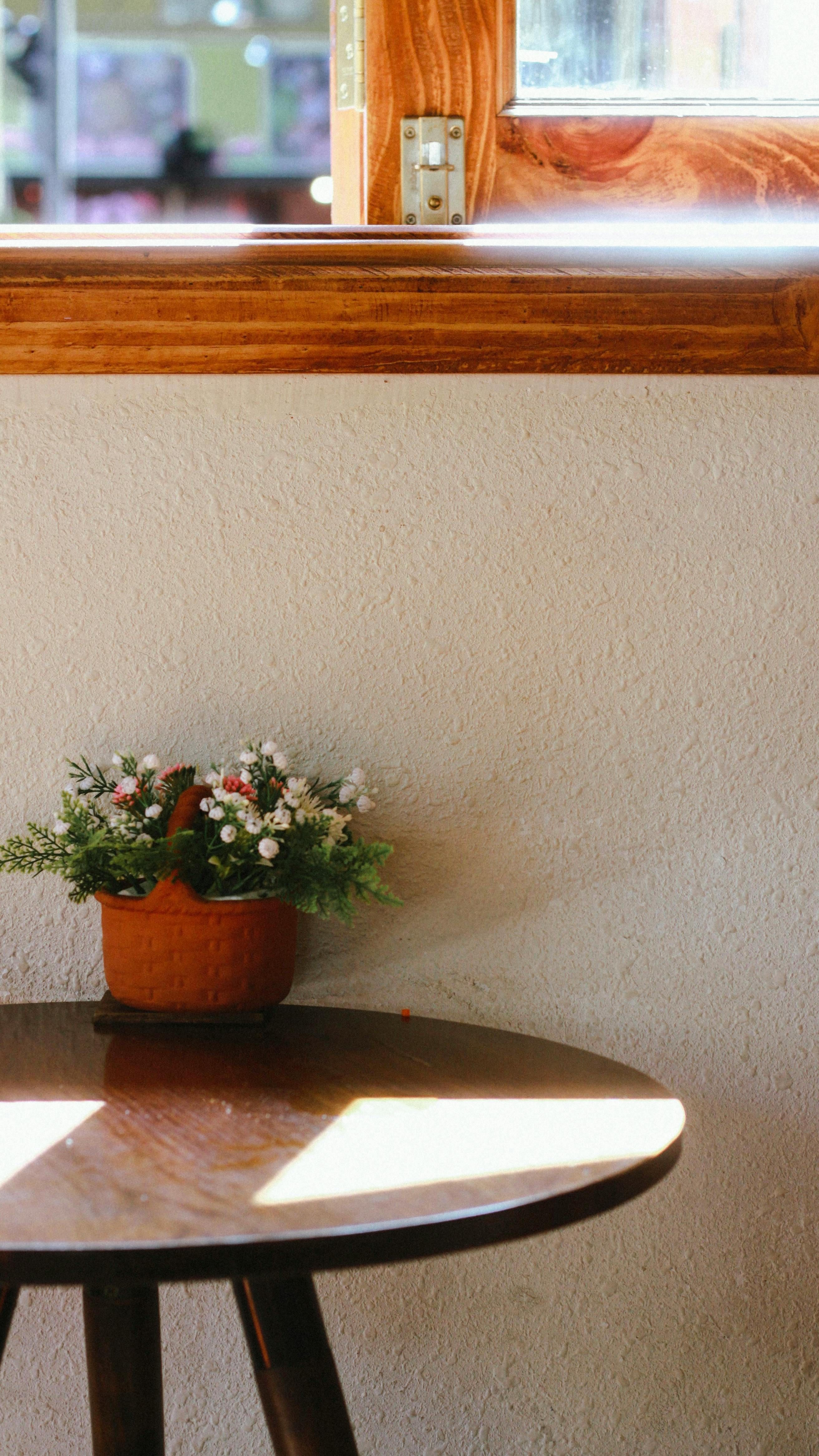 gratis Een klein bloemstukje op een zonnige houten tafel bij het raam zorgt voor een gezellige sfeer binnenshuis. Stockfoto