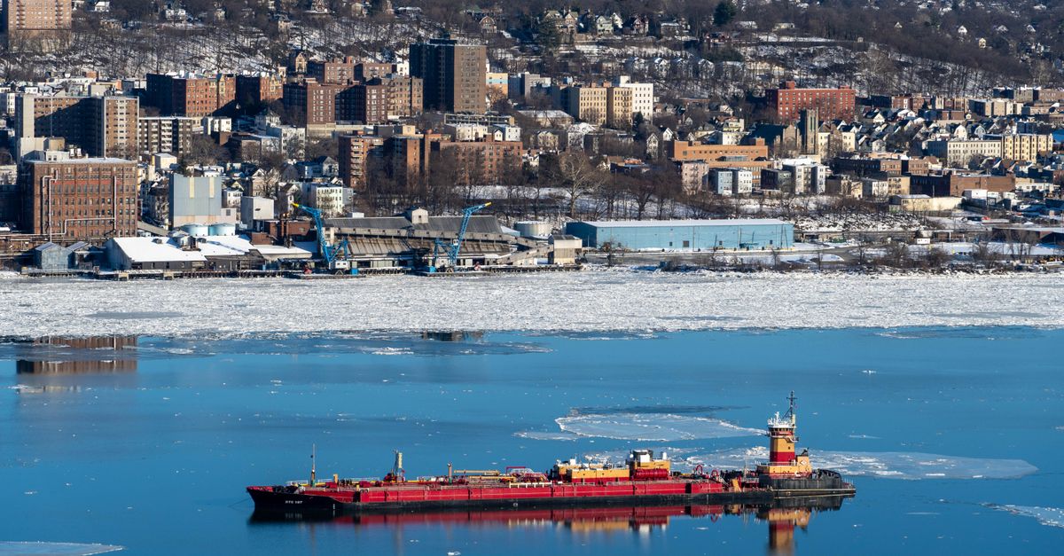 Aerial view of a coastal city with a cargo ship on icy blue water in winter.