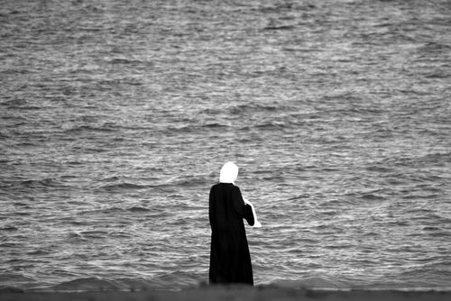 Free A person in traditional attire stands by the sea in Muscat, Oman, reflecting a mood of solitude. Stock Photo