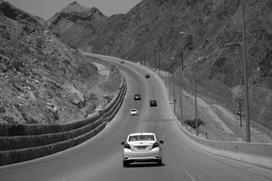 Economy car parked near a scenic road in Oman, suggesting car rental