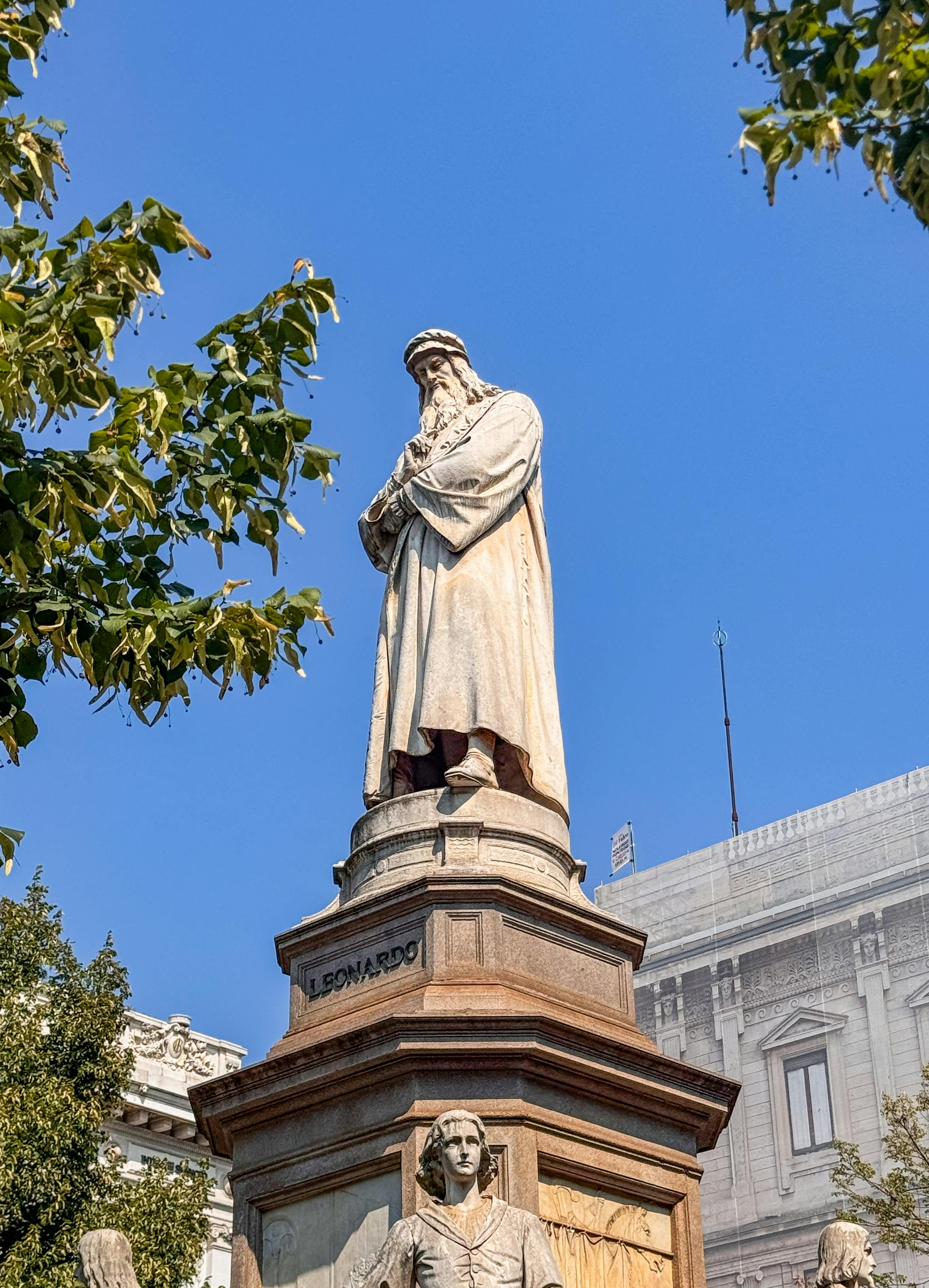 Statue of Leonardo da Vinci in Milan's Piazza della Scala on a bright day.
