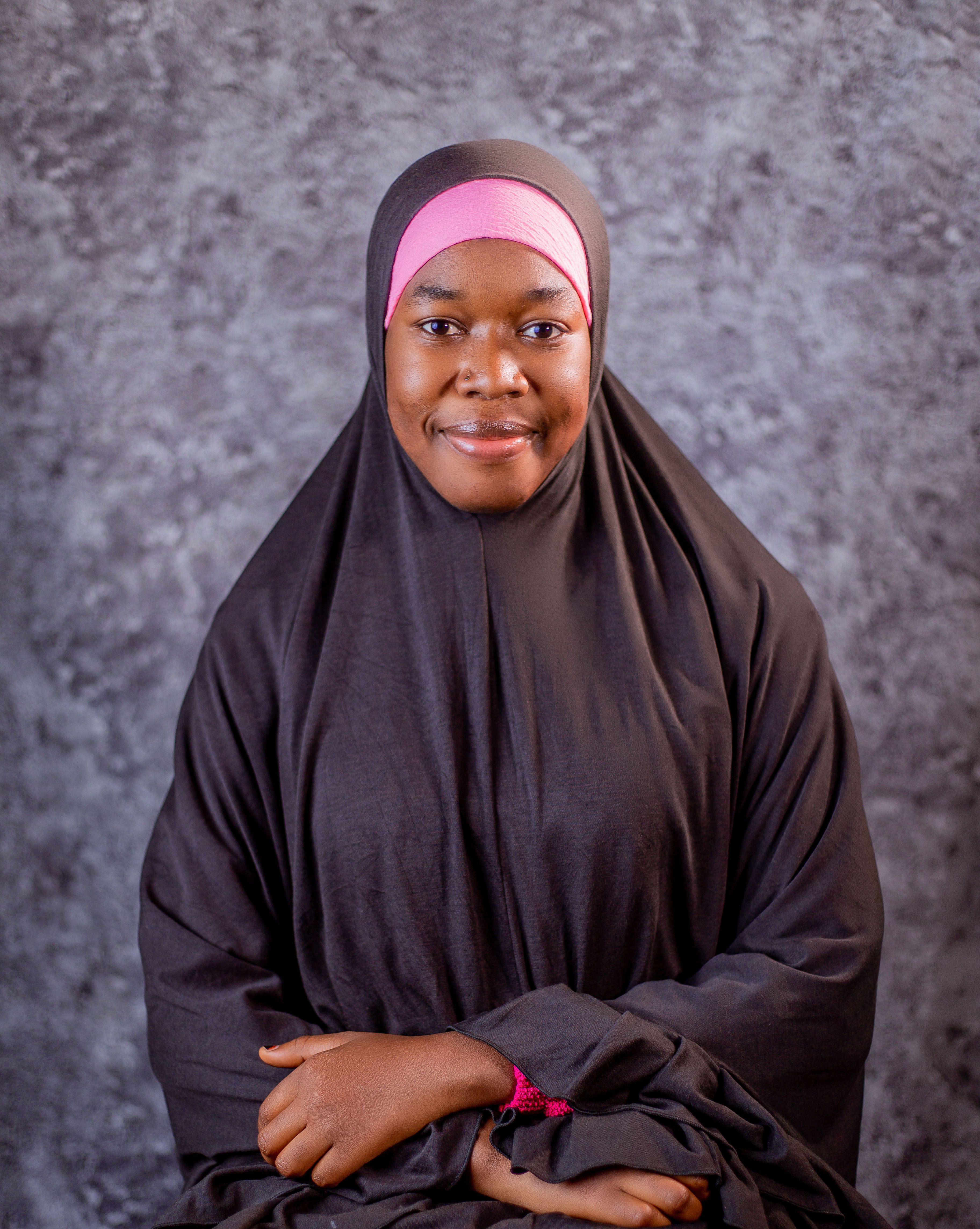 A confident woman wearing a hijab poses against a textured backdrop, conveying strength and grace.