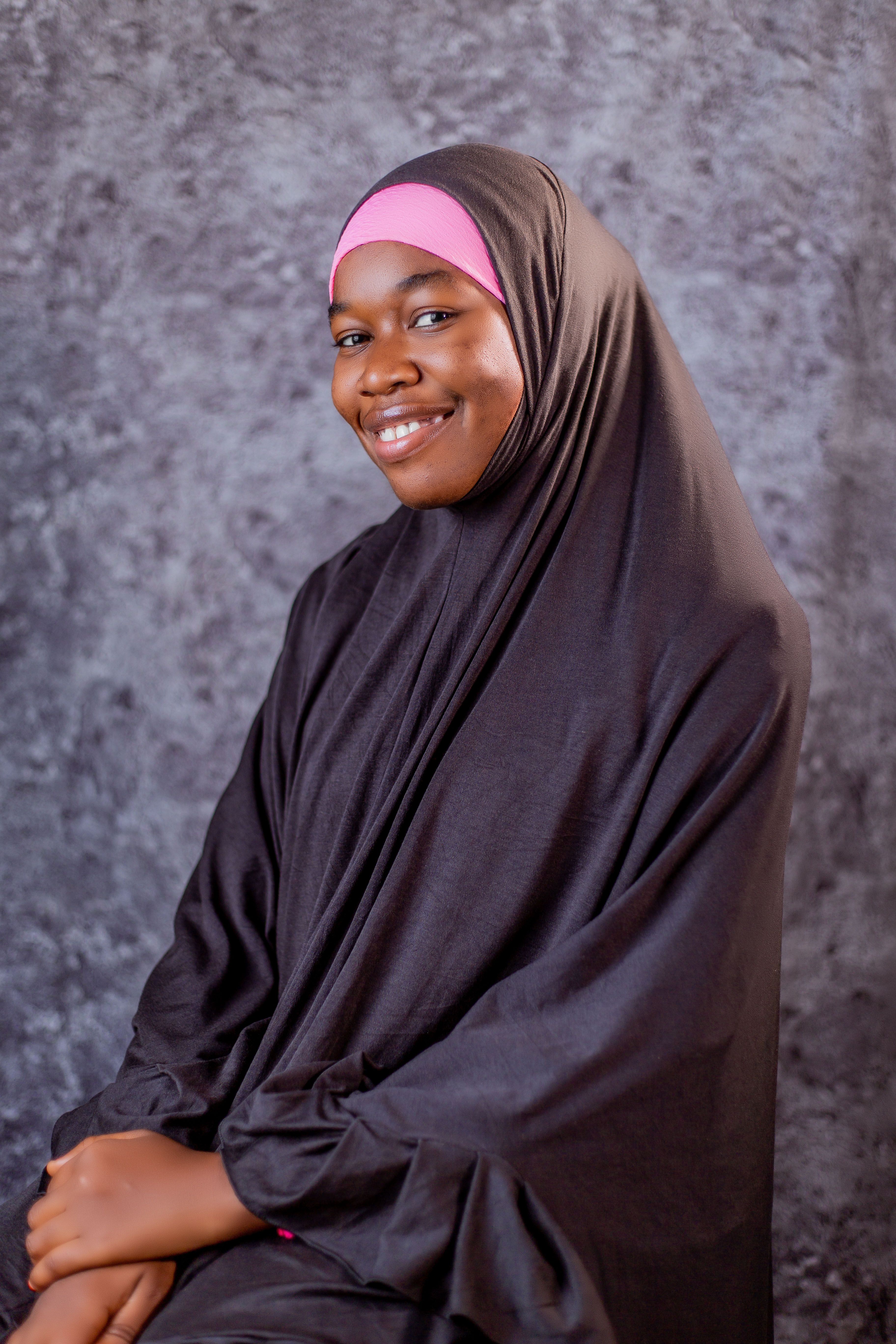 A serene portrait of a smiling woman wearing a hijab against a textured background.
