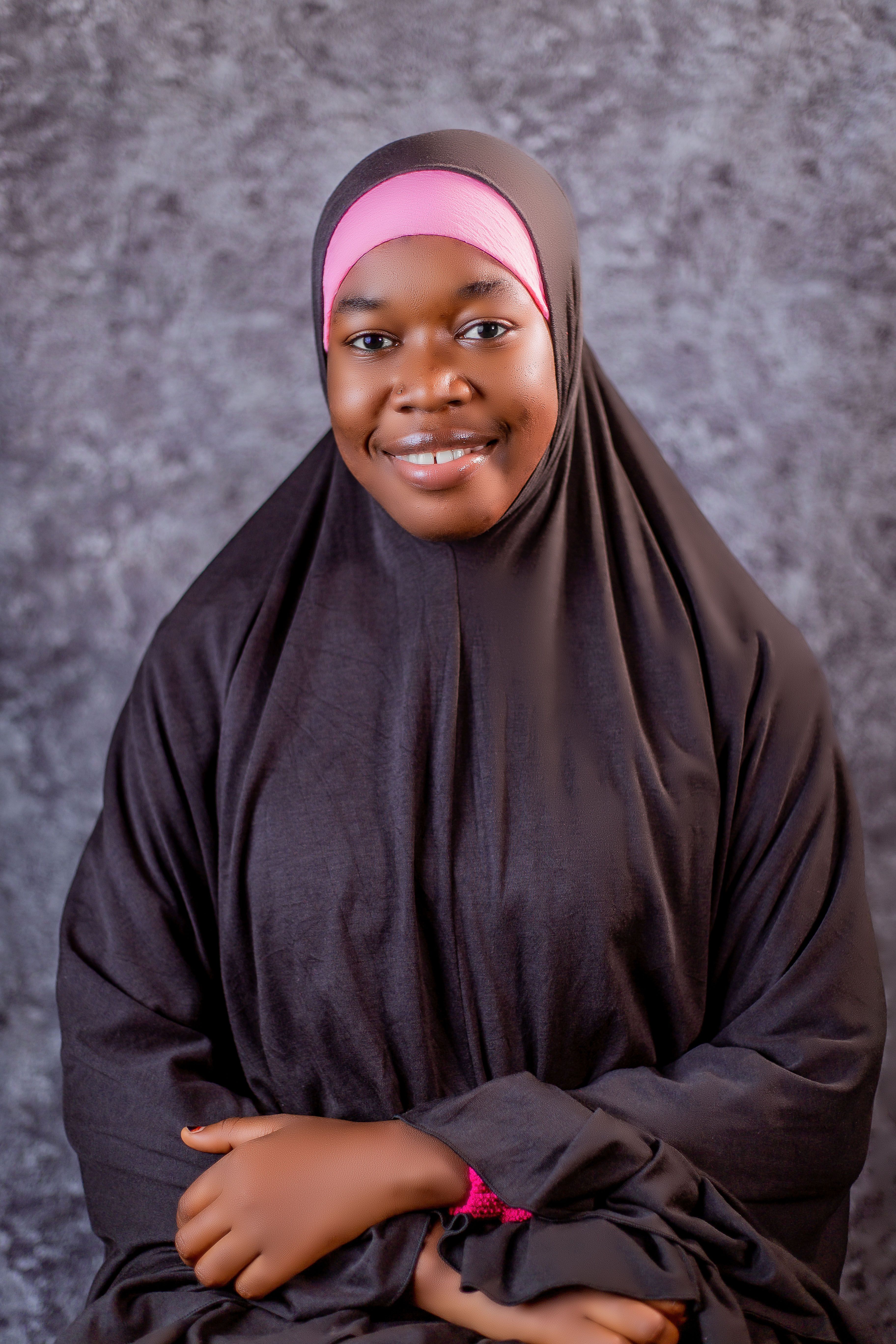 Charming portrait of a woman smiling in traditional hijab against a textured background.