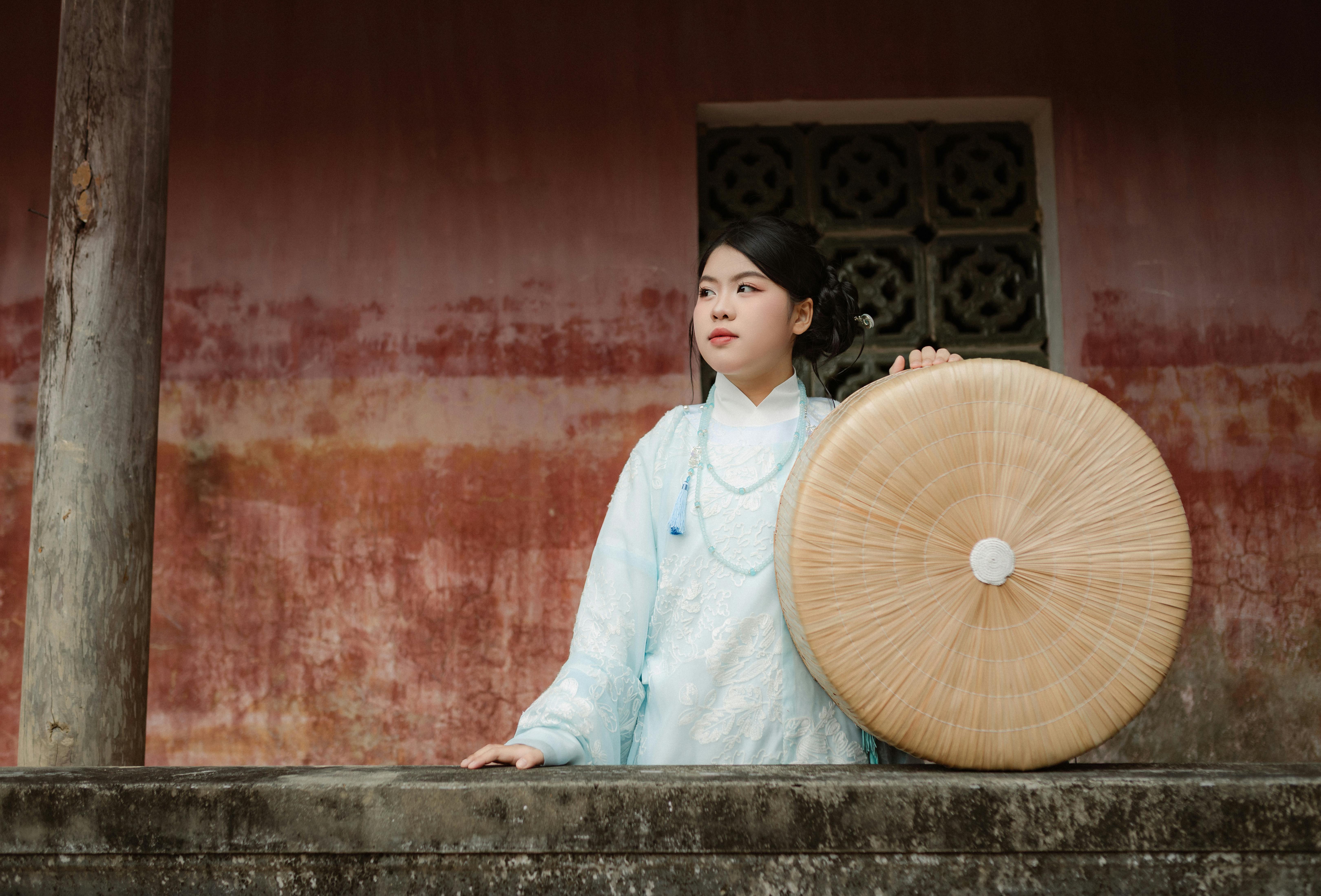 Young Vietnamese woman in traditional attire holding a round bamboo hat in Hội An.