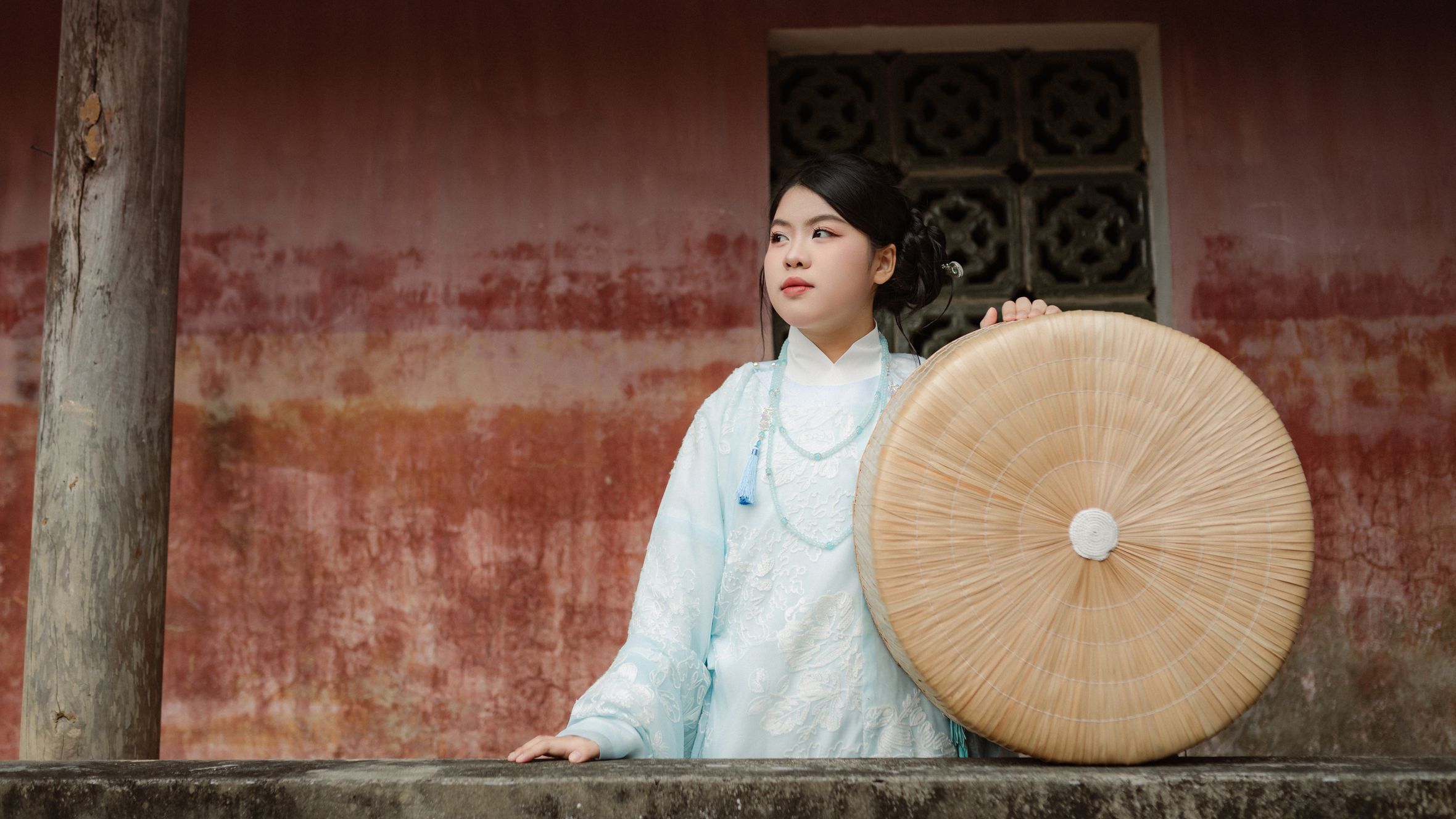 Young Vietnamese woman in traditional attire holding a round bamboo hat in Hội An.