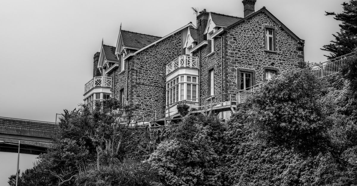 Black and white image of a historic stone house with lush foliage in Brittany.
