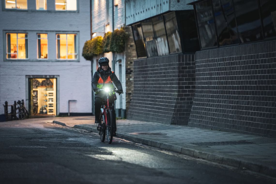 Cyclist commuting through a city at night wearing reflective gear and a helmet