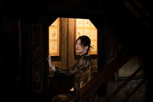 A woman in vintage attire poses gracefully in a dimly lit, ornate interior setting.