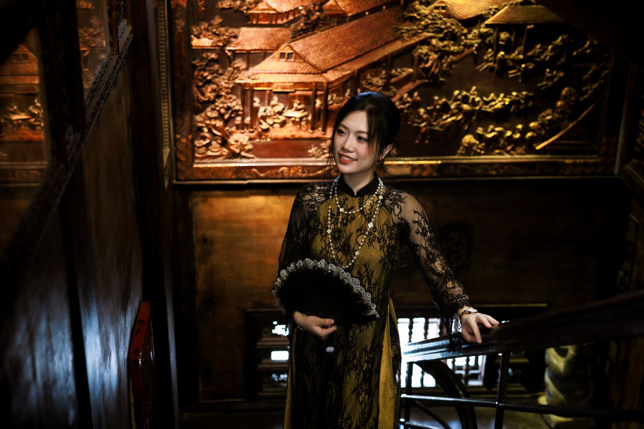 a woman in traditional asian attire poses indoors with ornate wooden c