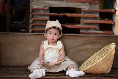 Free Charming portrait of a child in a white dress and hat, holding a fan beside a wicker basket. Stock Photo