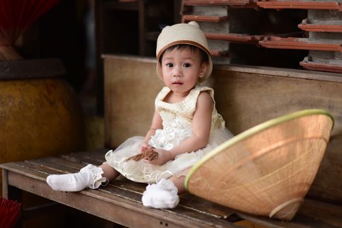 Free Charming toddler girl wearing a traditional Asian outfit, sitting with a conical hat. Stock Photo