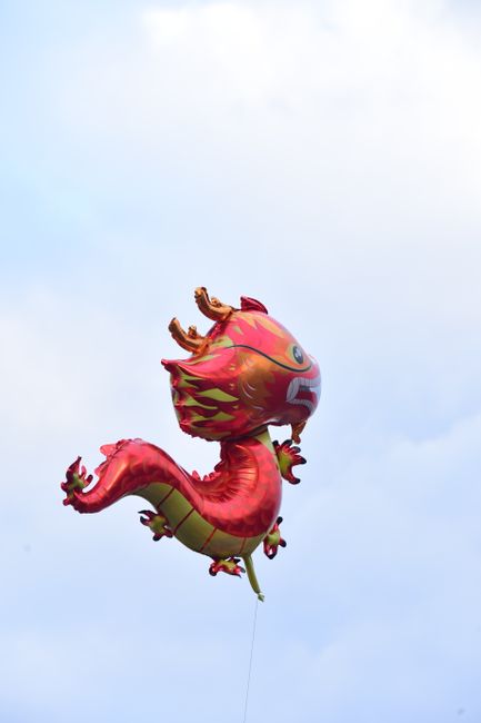 A vibrant dragon-shaped balloon floating against a clear blue sky, showcasing lively designs and colors.