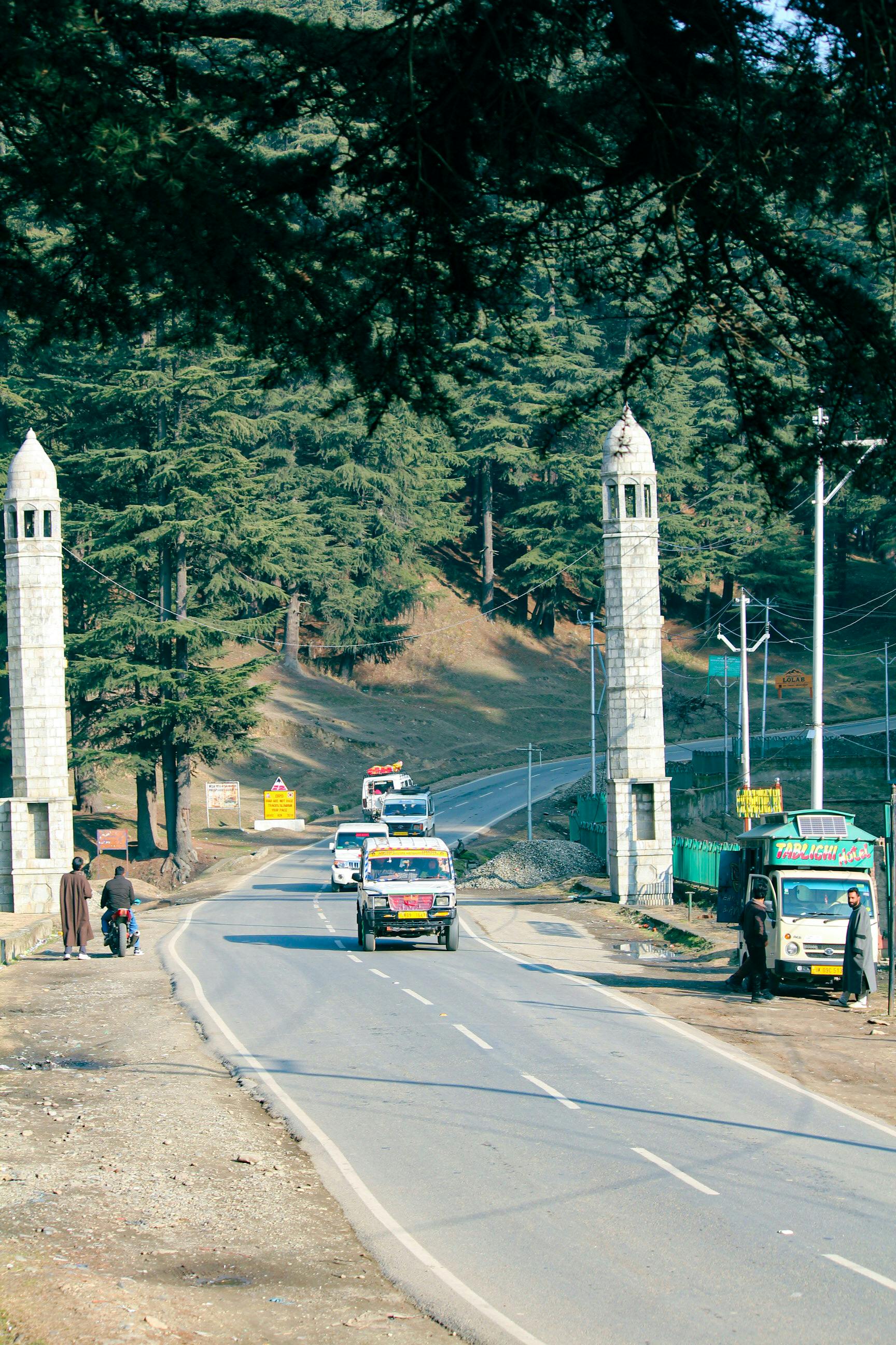 Kostnadsfria En naturskön väg med fordon som passerar genom ett skogsområde, inramat av höga stenpelare. Stock foto