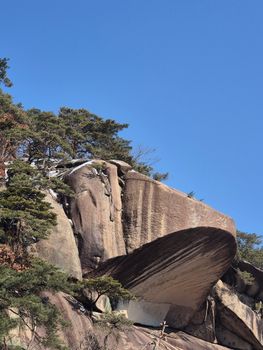 Massive rock formation with trees under a bright blue sky, showcasing natural beauty.
