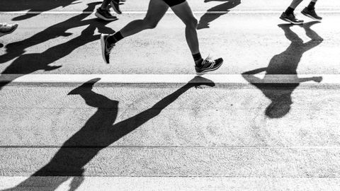 Black and white photo capturing the shadows of runners on a city street during a race.