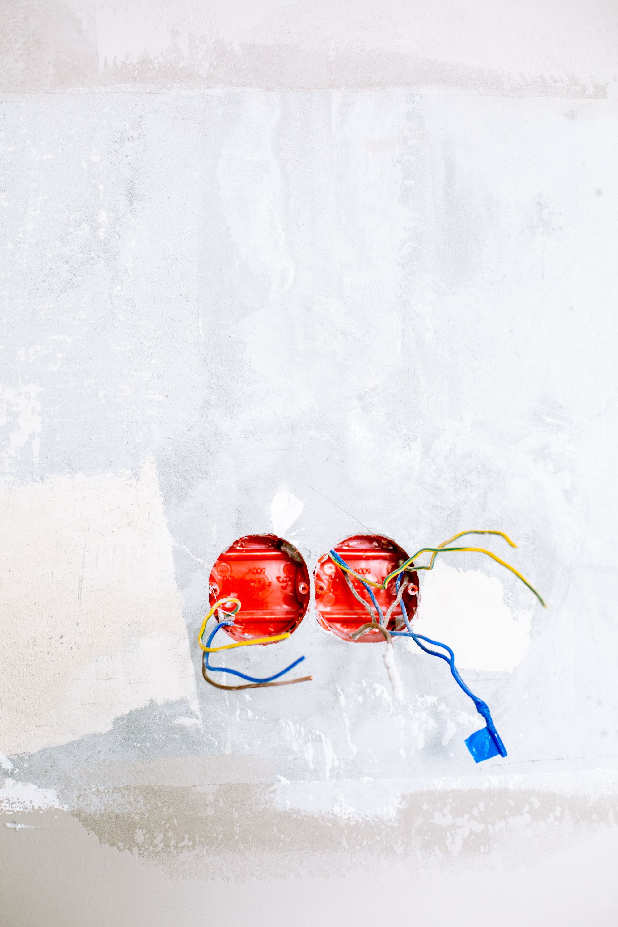 An unfinished white wall with two exposed red electrical boxes and loose coloured wires hanging out.