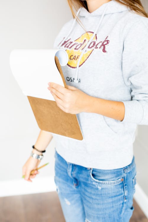 Person Wearing Gray Hoodie While Holding a Notepad
