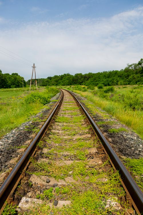 Free Curved railway tracks blending into lush green landscape under a bright blue sky. Stock Photo
