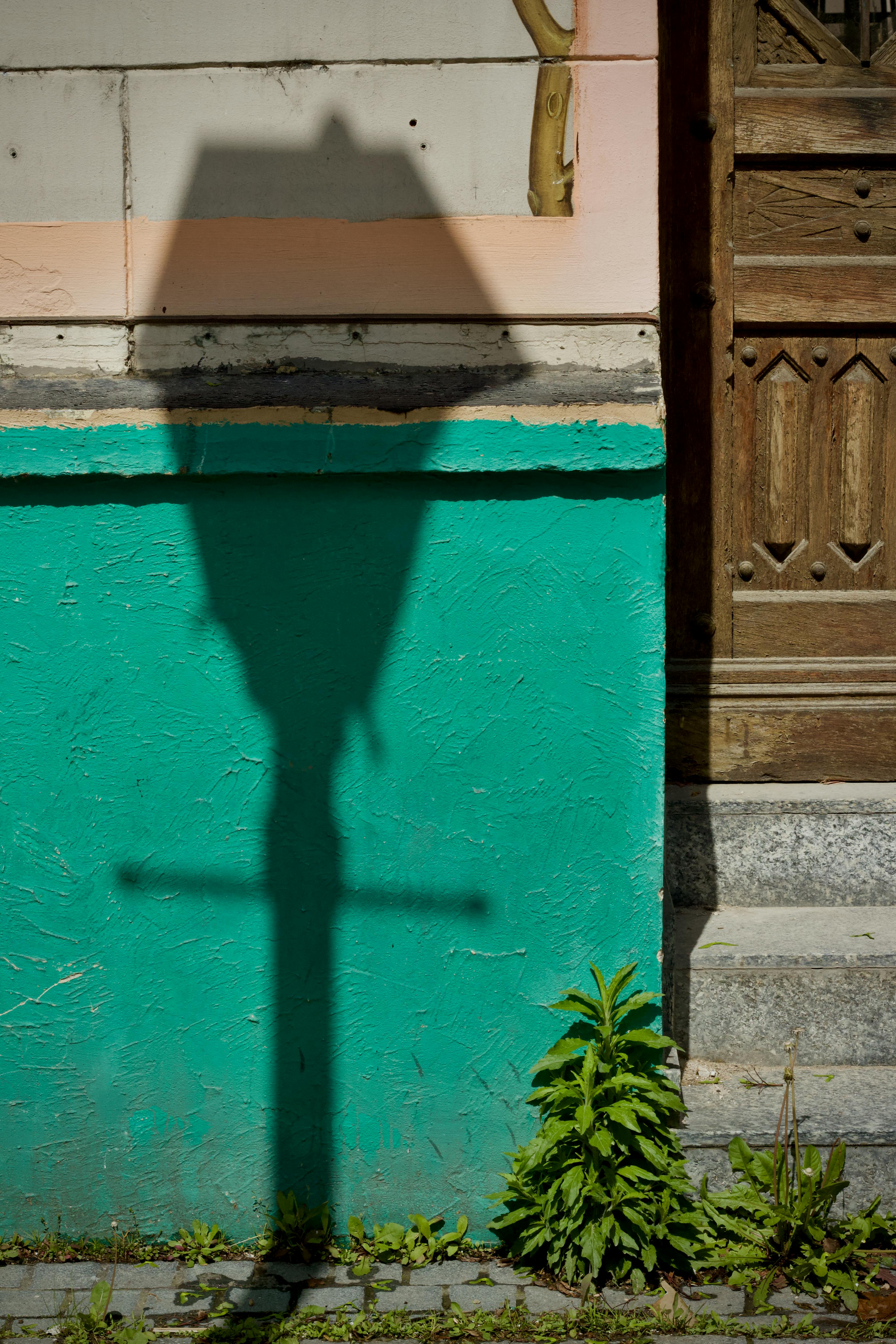 Gratis Bayangan lampu jalan di dinding berwarna biru kehijauan yang cerah dengan detail pintu kayu. Foto Stok