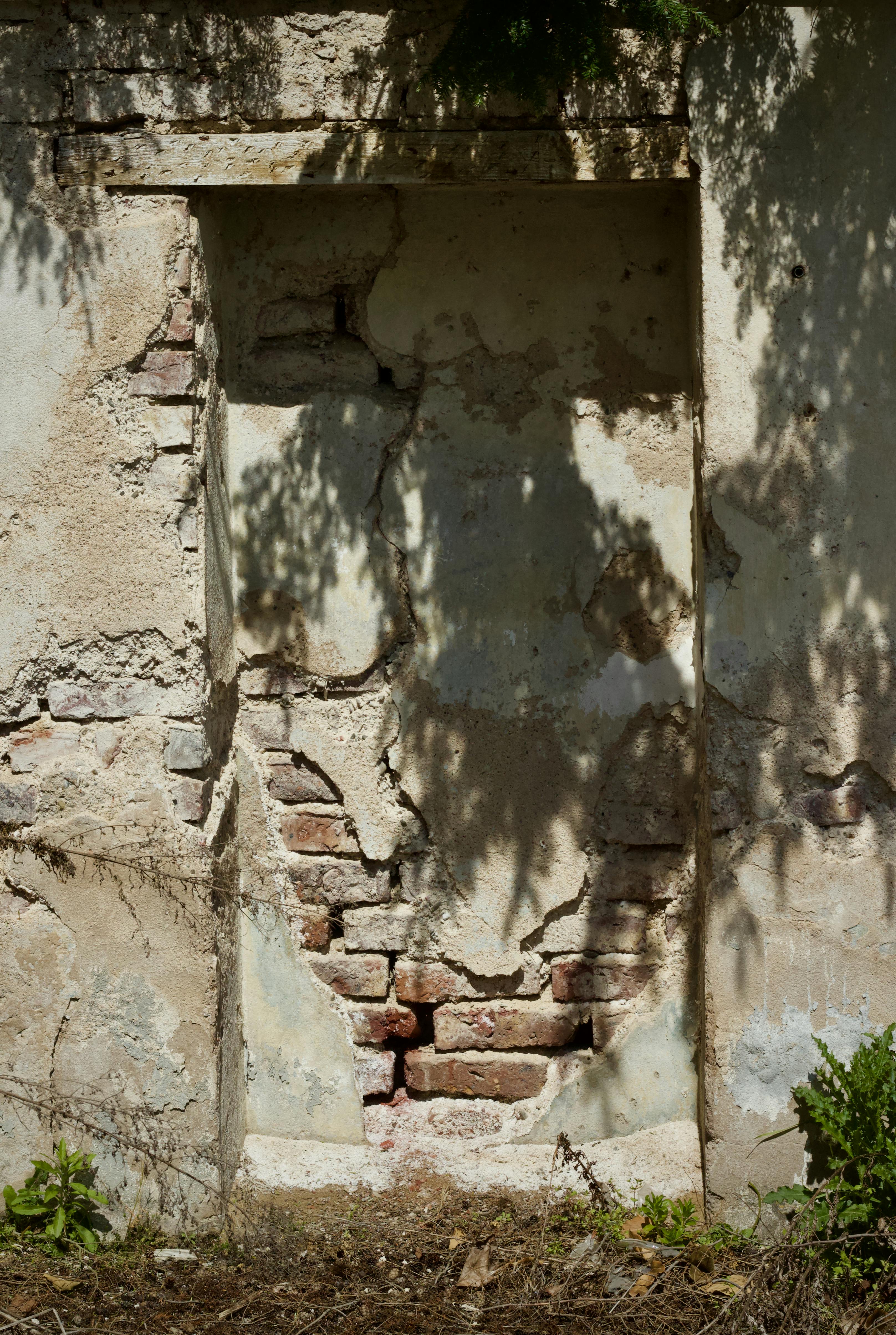 Gratis Sollys kaster skygger på en smuldrende murvegg med avskallende puss, og avslører en værbitt tekstur. Arkivbilde