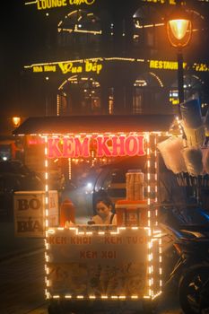 Colorful ice cream cart on a bustling Hanoi street at night, offering delicious treats to passersby.