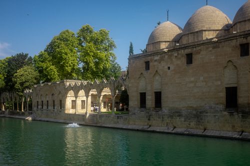 Free Scenic view of historical stone architecture and peaceful pool surrounded by lush greenery under bright daylight. Stock Photo