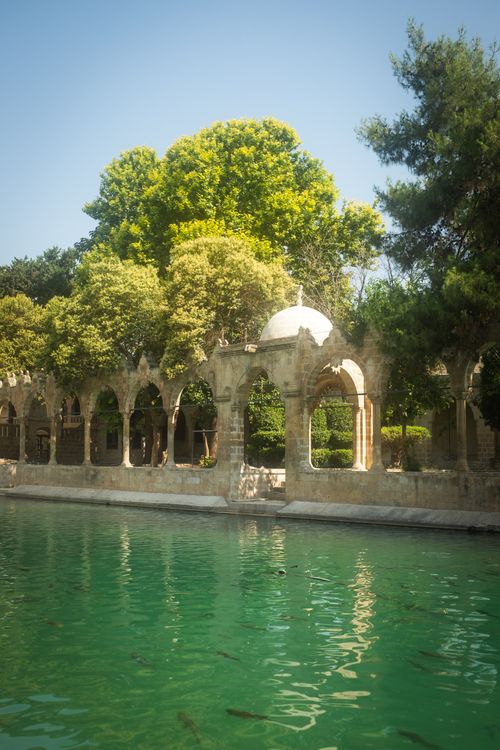 Free Tranquil scene of ancient arched architecture by a turquoise pond surrounded by lush greenery. Stock Photo