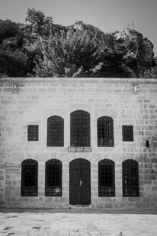 Free Black and white image of a historic building with arched windows and a rocky backdrop. Stock Photo