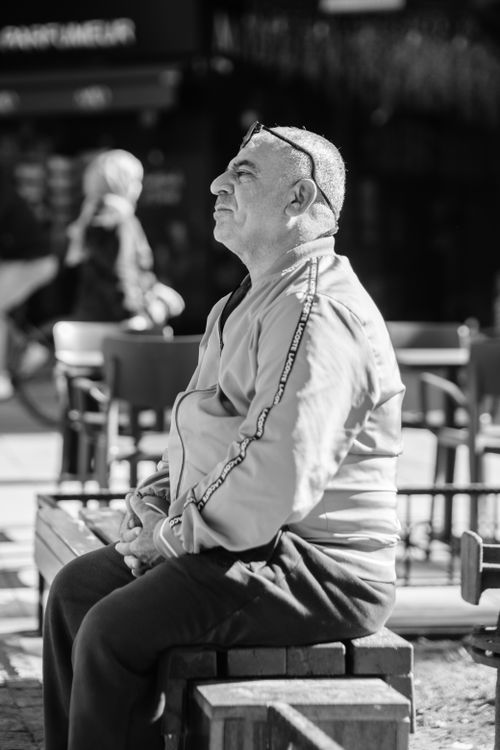 Free A contemplative man sits on a bench in a public outdoor space in black and white. Stock Photo