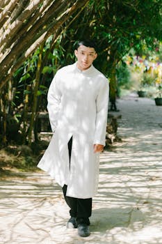 A young man walks through a serene bamboo grove wearing traditional white attire, enveloped in natural light.