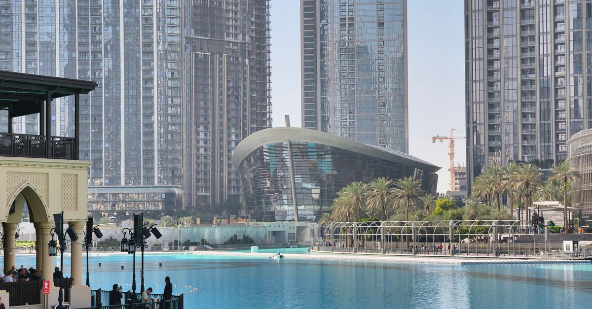 View of Dubai Opera House and surrounding skyscrapers reflecting in the water.