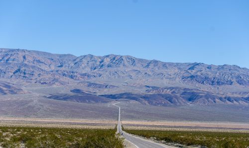 Free A long, straight road leading through a vast desert towards distant majestic mountains under a clear blue sky. Stock Photo