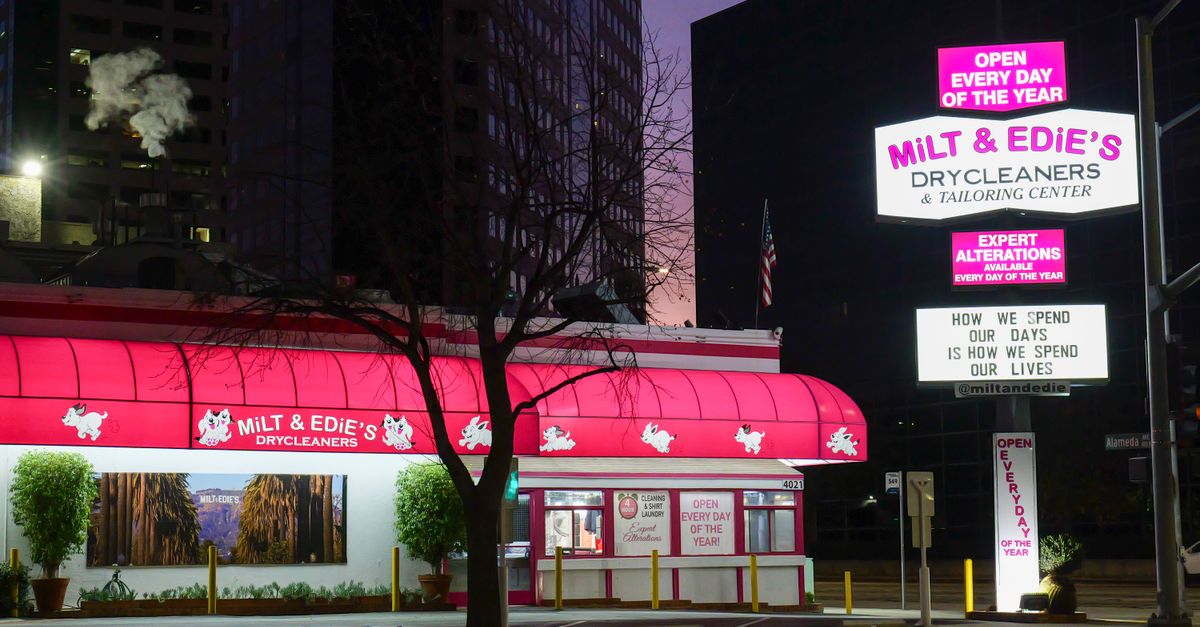 Milt & Edie's Drycleaners illuminated at night in bustling USA cityscape.