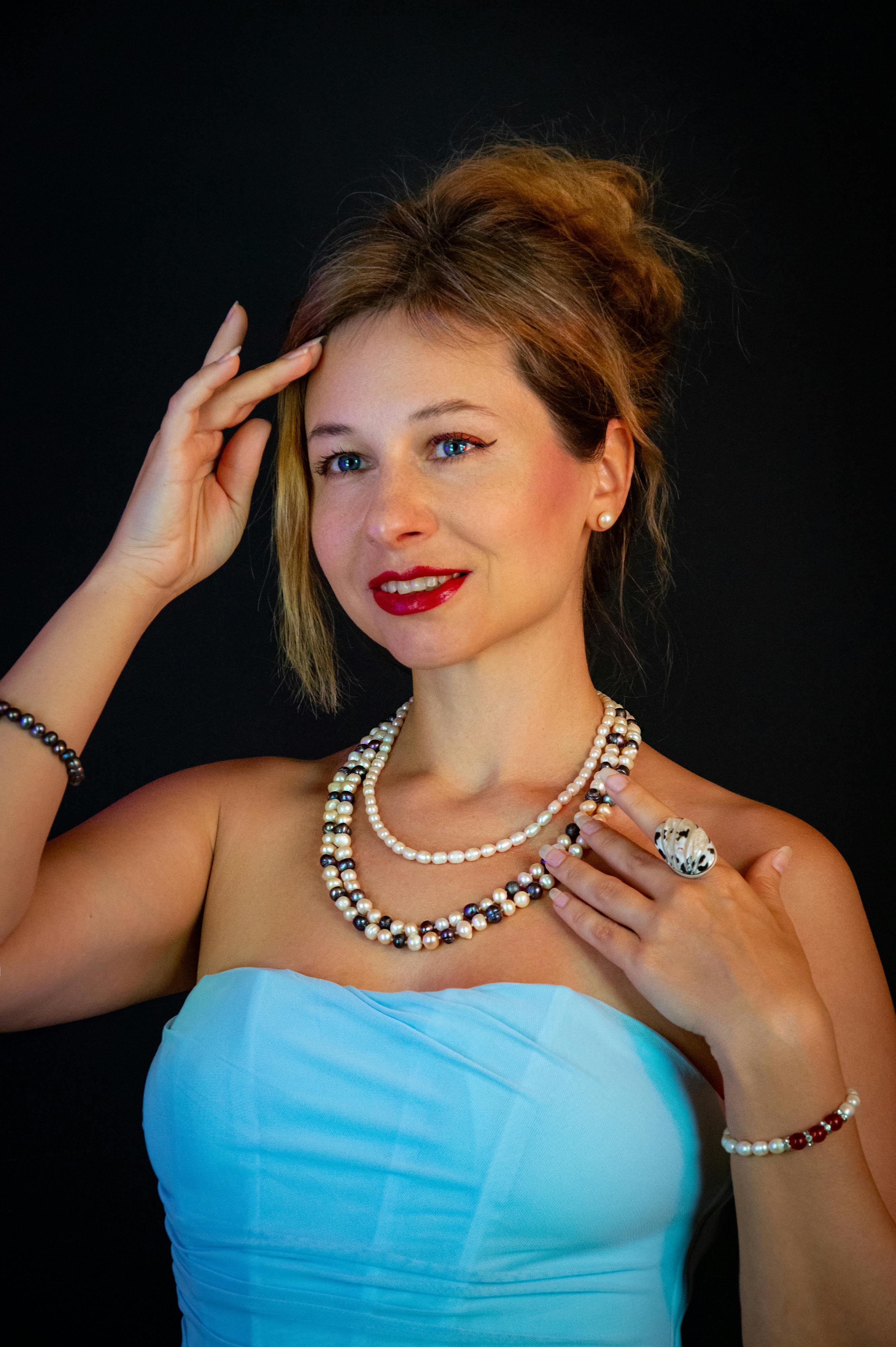 ฟรี หญิงสาวผู้สง่างามในชุดเดรสเกาะอกสีฟ้า อวดเครื่องประดับมุกบนพื้นหลังสีดำ คลังภาพถ่าย